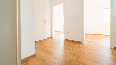 Helle leere Wohnung mit Holzboden und weißen Wänden, Blick auf Flur und offene Türen.